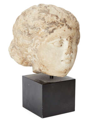 A marble female head
		After the Antique
		Her hair swept back from her forehead in waves, then drawn into a bun, 12.5cm high
		 
		Provenance:
		From th